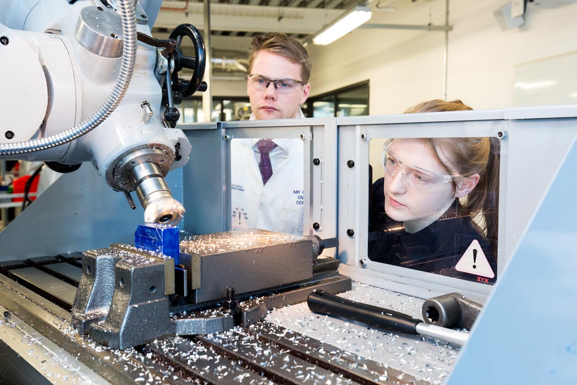 female engineering student working on a milling machine is observed by an instructor