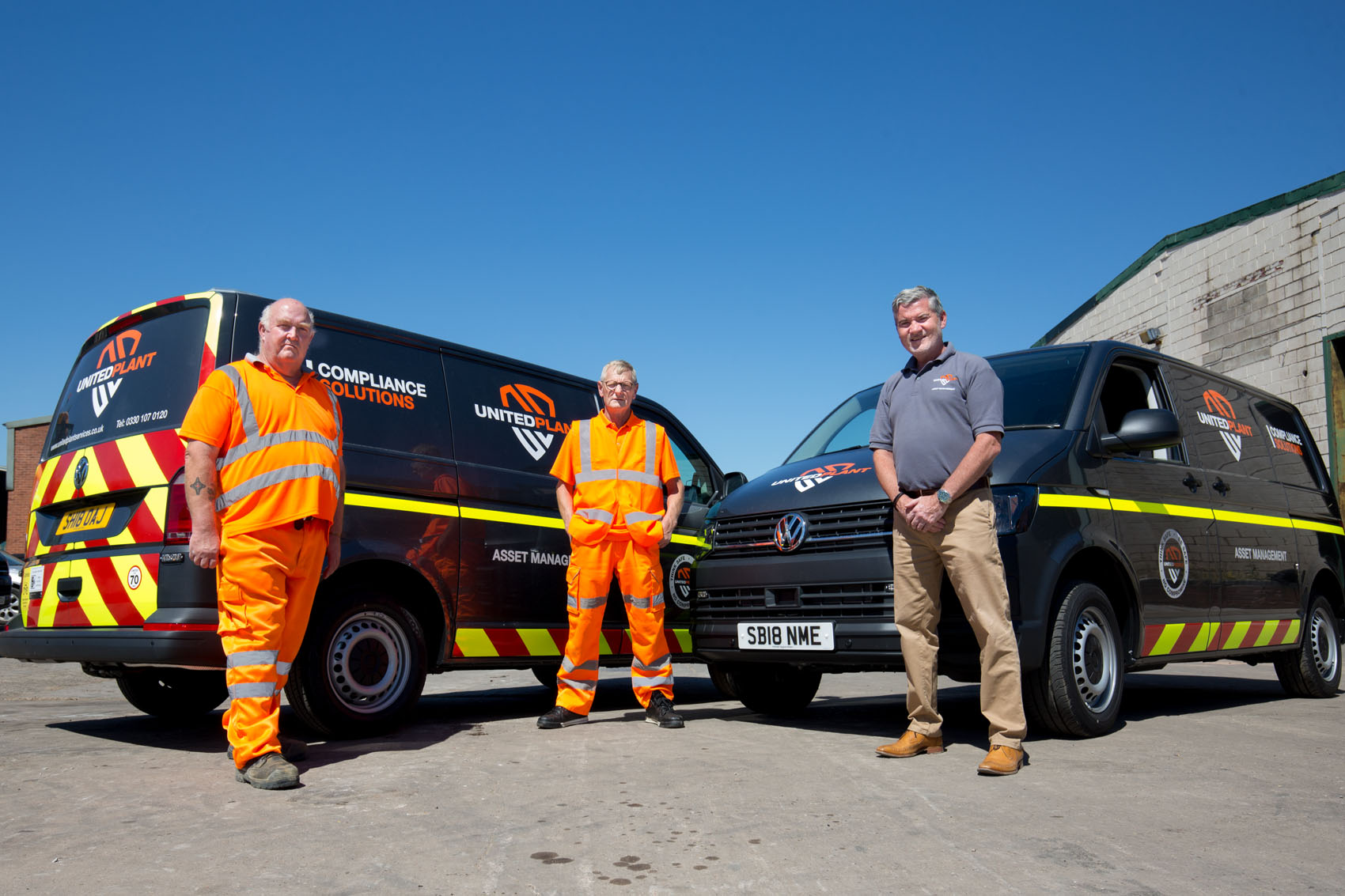 Two enginners in orange overallsand the director in fron of new vans