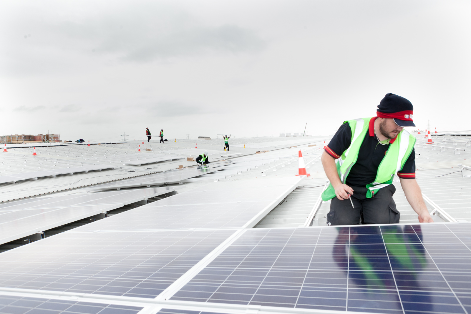 Solar array Castle Donington covering a huge roof expanse with worker in foreground and group of workers in distance