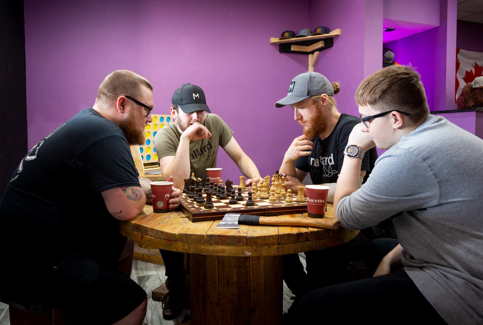Chess player sitting at a round table with two spectators and an axe in the table