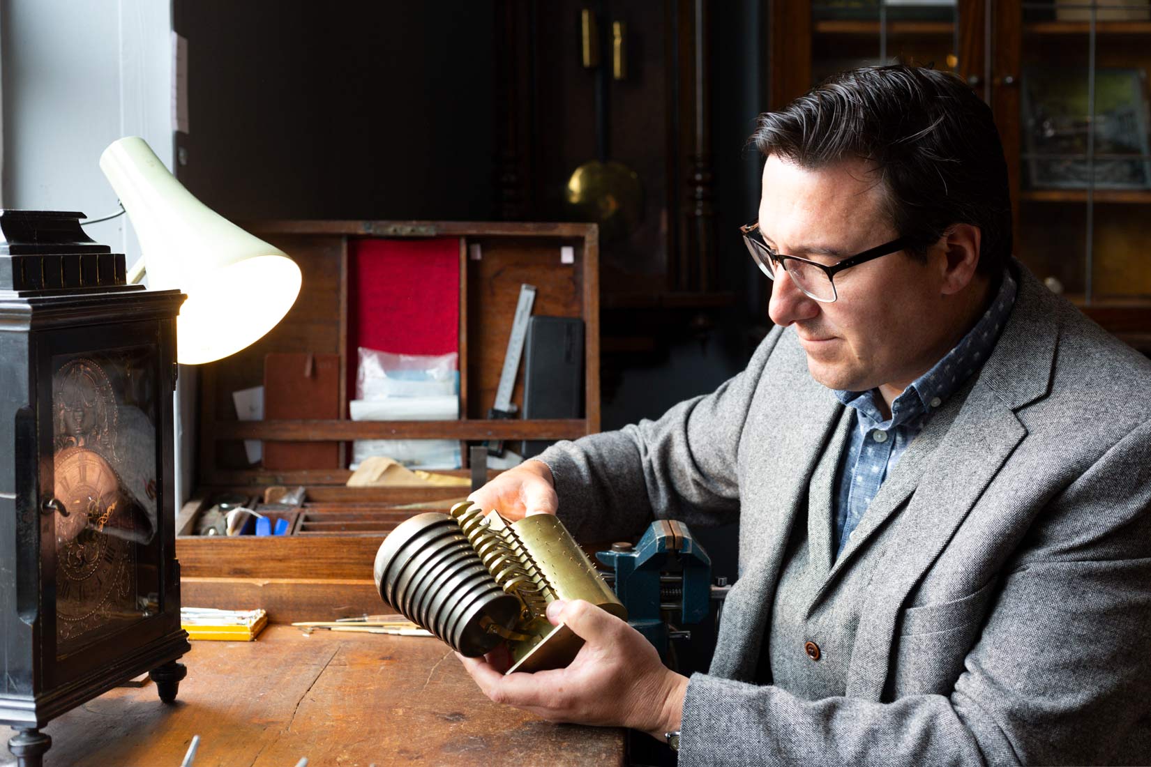 Clockmaker inspecting cylindrical brass drum 