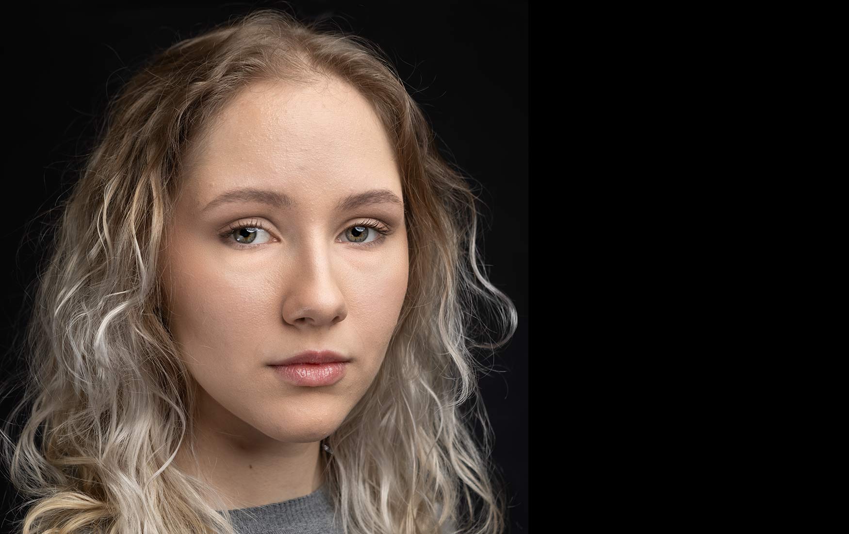 Actor headshot closely cropped portrait of a young female actor with blond streaked hair and a soulful look against a black background