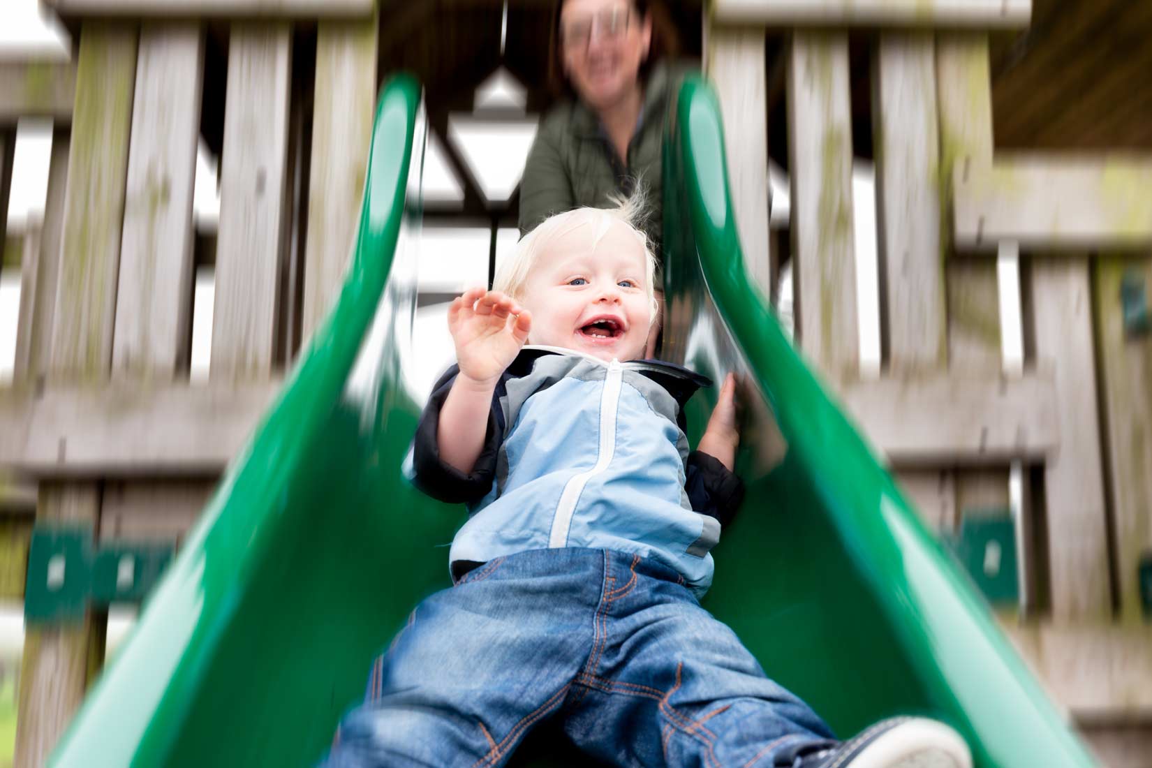 Editorial photography of a laughing toddler in blue on a green slide