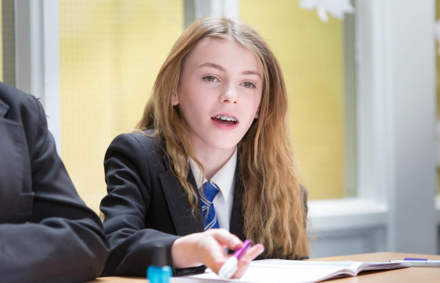 Girl in school blazer and tie studying in class sitting at desk with pen in hand