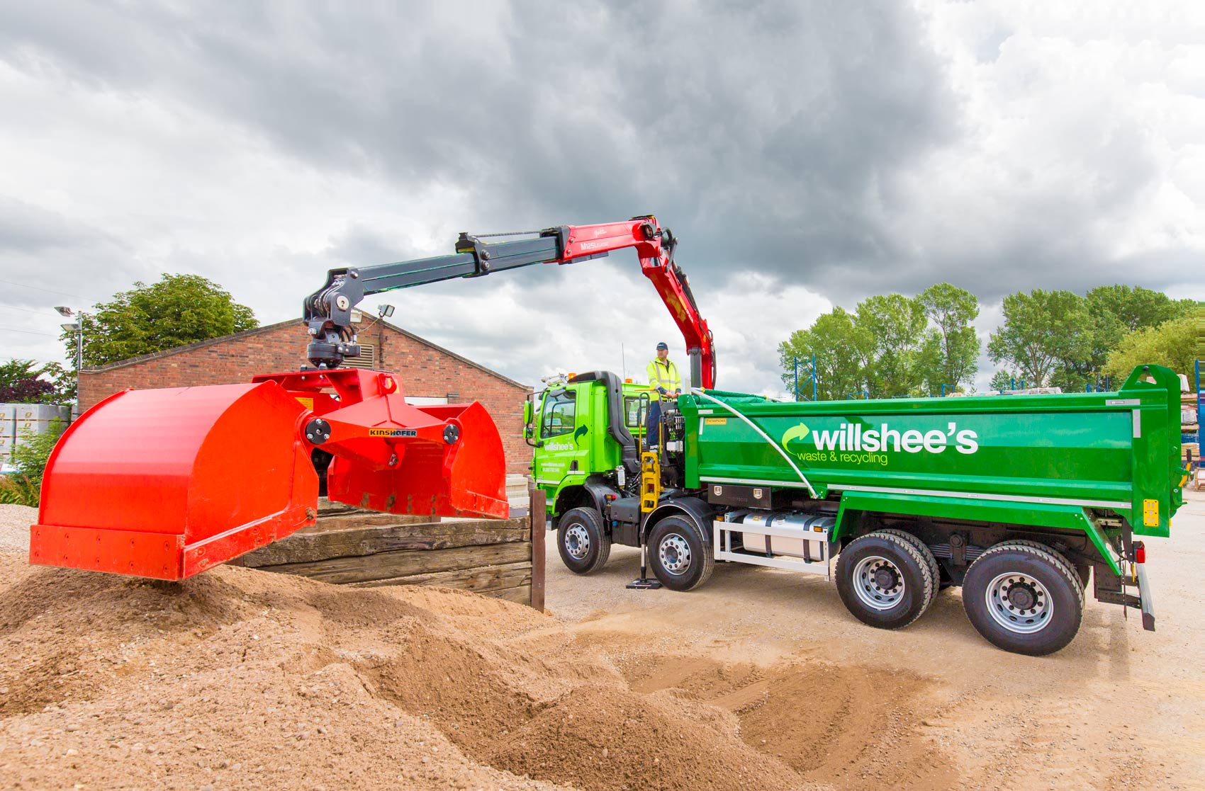 Construction Photography of a green grabber truck wit ha bright red bucket about to grab a load of gravel
