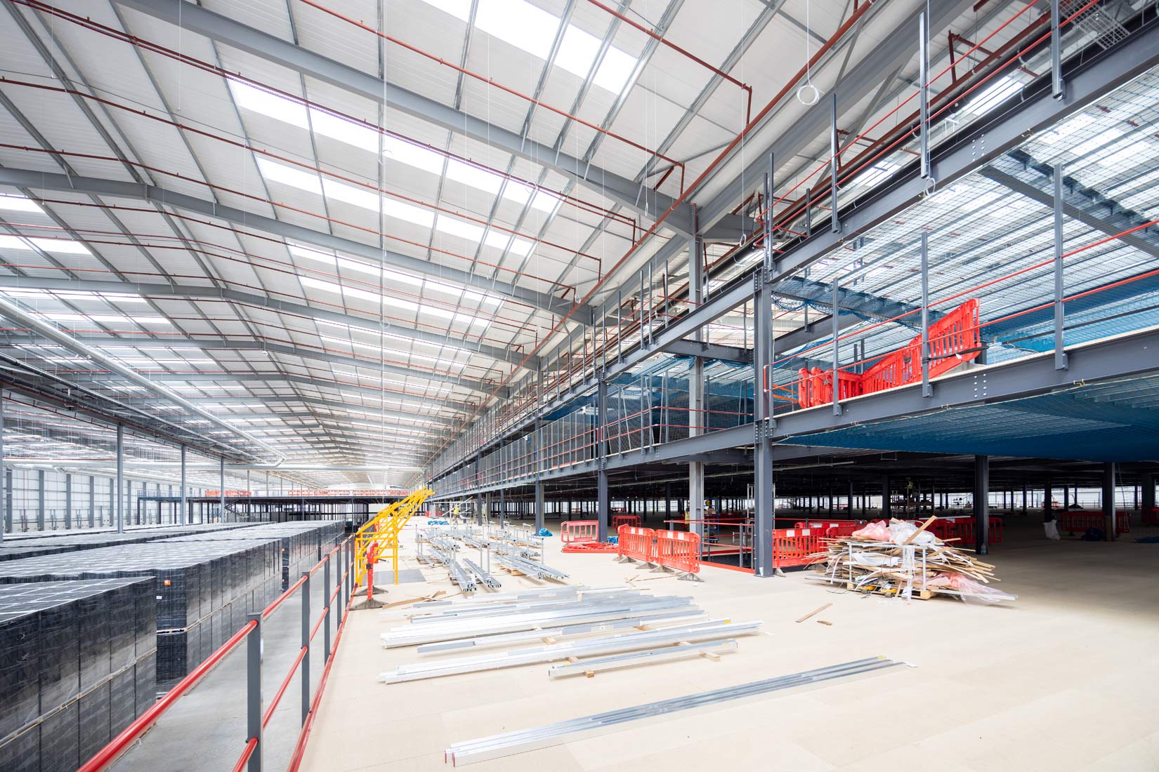 Construction Photography of a mezzanine in a large warehouse, beige wood chip boards in front of steel work and red barriers   