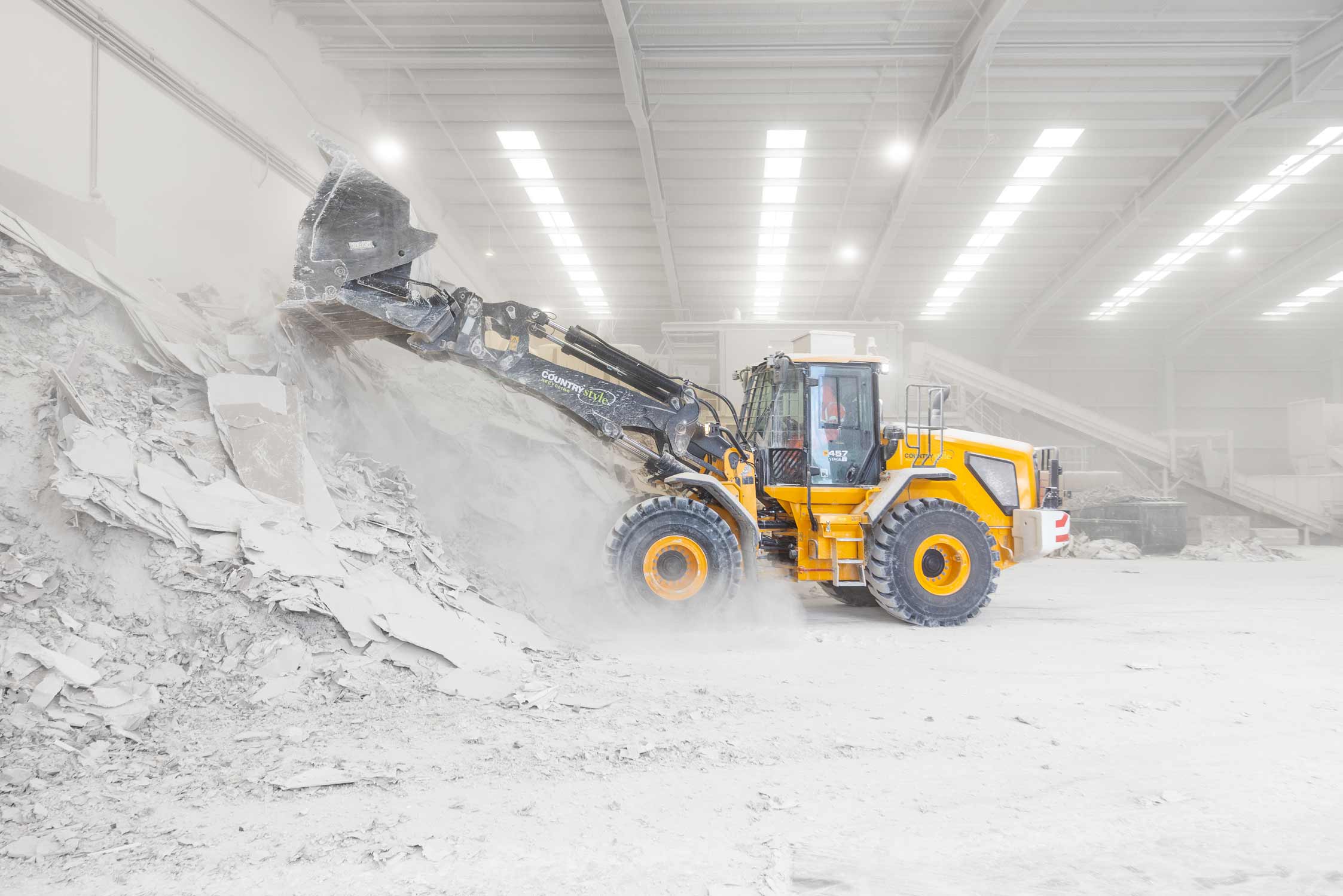 A yellow front loader plant equipment pushes and scoops plasterboard into a mound
