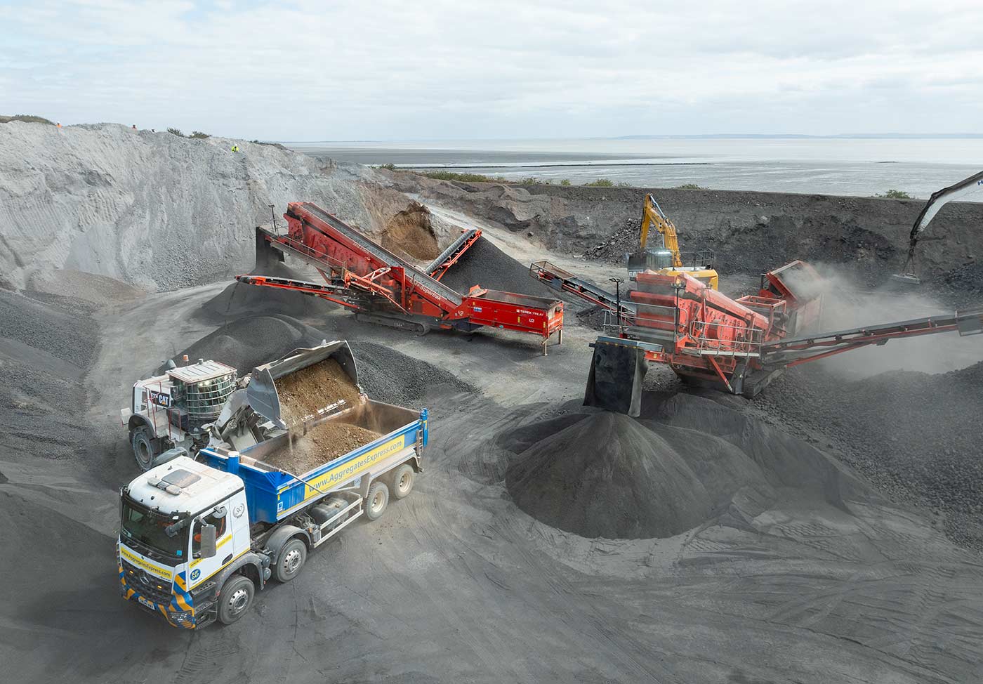A truck being loaded with Asphalt production heavy plant in the background